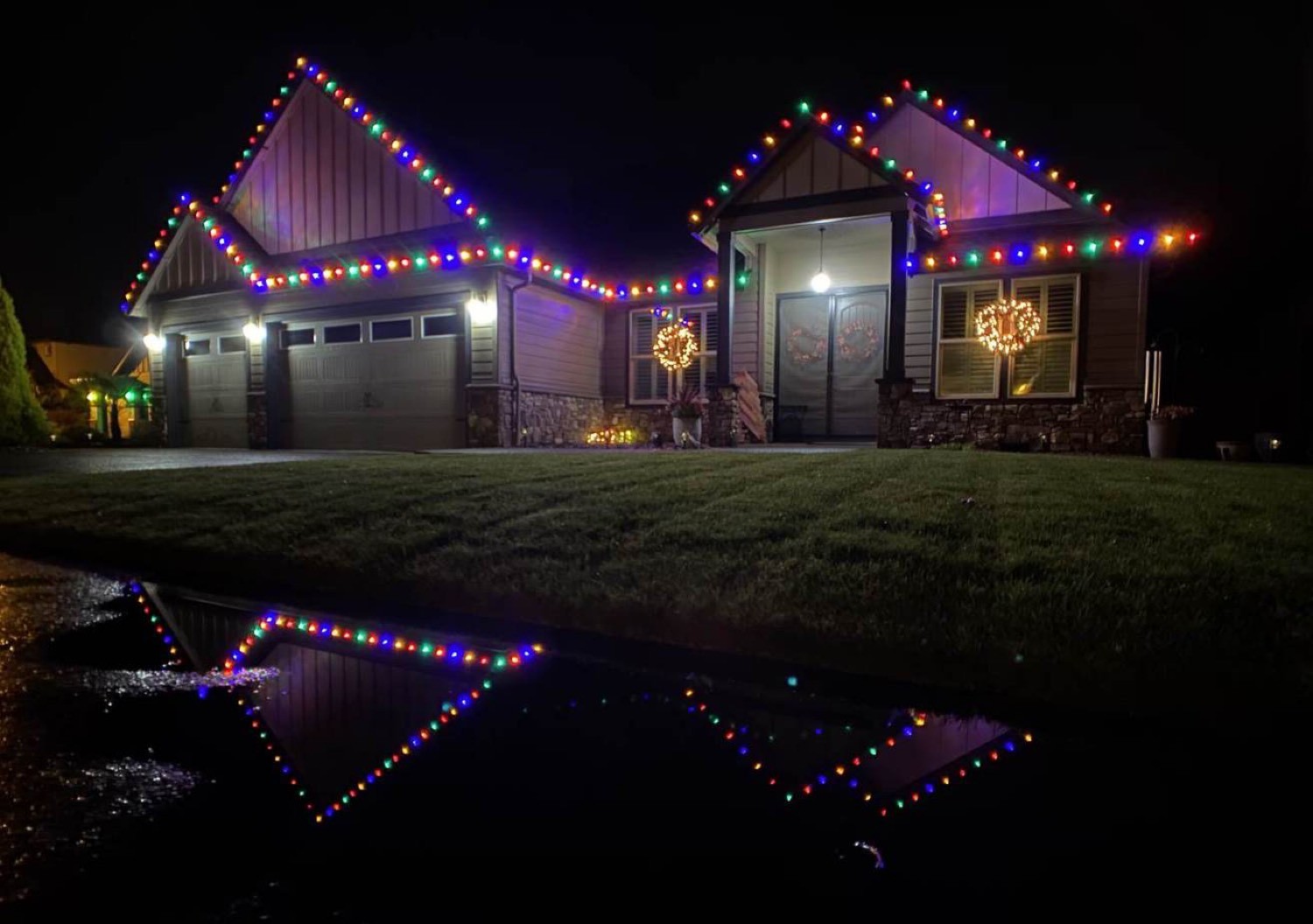 Classic color C9s on a two-peak home, wreaths on the windows, lights reflected in the street